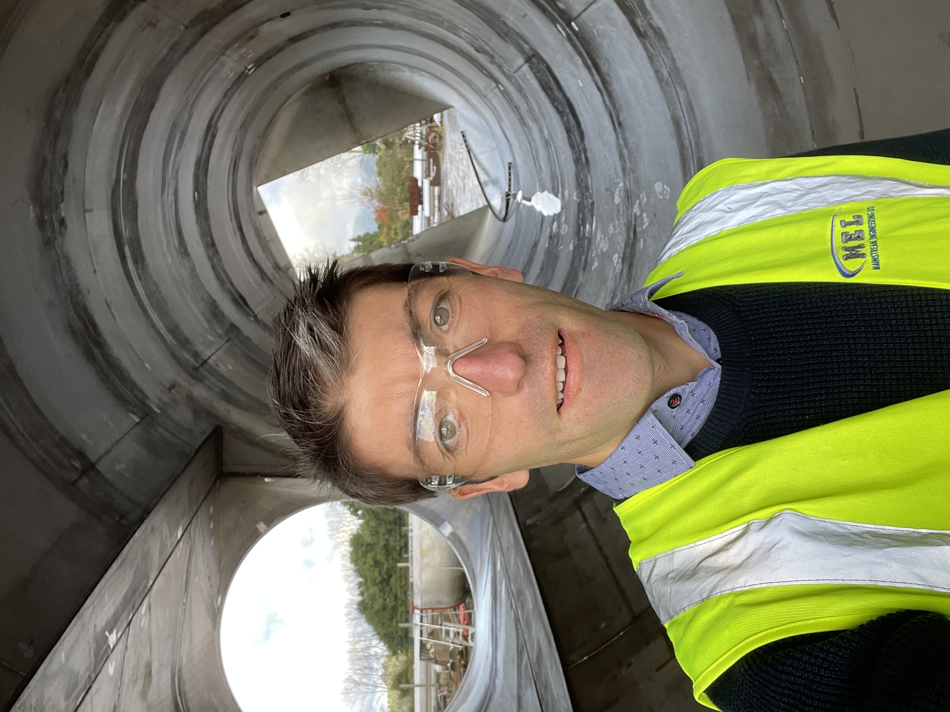 Chris Lines on site in high-visibility gear and safety glasses, standing inside a large fabricated duct section